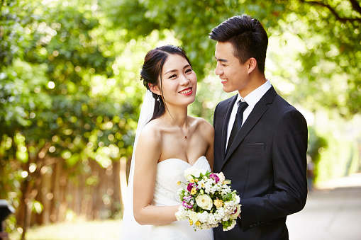 outdoor portrait of asian bride and groom looking at camera smiling.