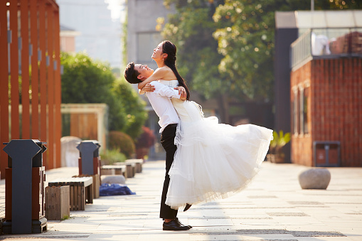 asian newlywed bride and groom celebrating marriage in parking lot.