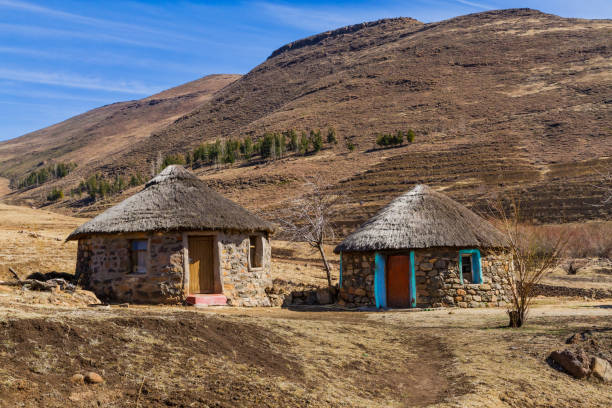 Leribe, Lesotho - August 10, 2016: Traditional Basotho stone huts with colorful doorways, thatched roofs, and mountains on a sunny winter day in a remote rural area of this southern Africa kingdom