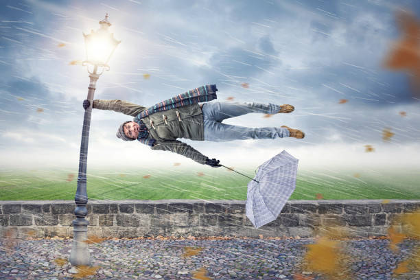 Man gets blown away by a storm Man flying away horizontally in a storm while holding on to a street lamp with one hand. The other hand is holding an upended umbrella. natural disaster photos stock pictures, royalty-free photos & images