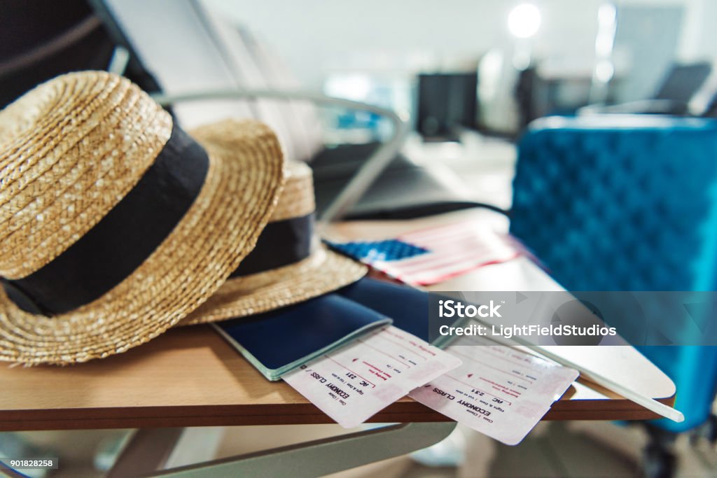 traveling equipment on chair at airport close up view of hats, passports with tickets and american flag on wooden chair at airport Airplane Ticket Stock Photo