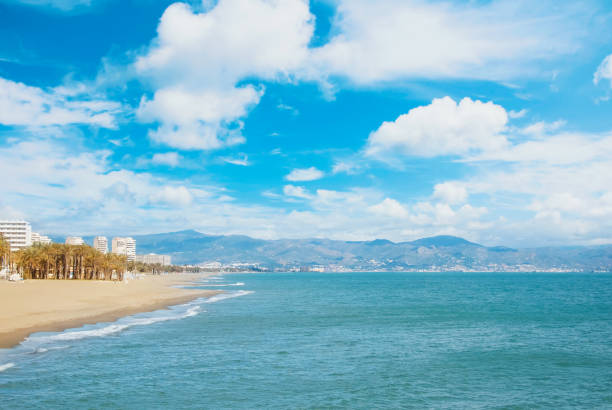 Panoramic view to a perfect dreamy paradise white yellow sandy bay beach by the blue sea and dramatic cloudy sky with palms and hotels, lagoon and mountains at the background, winter vacation concept. Panoramic view to a perfect dreamy paradise white yellow sandy bay beach by the blue sea and dramatic cloudy sky with palms and hotels, lagoon and mountains at the background, winter vacation concept. torremolinos beach stock pictures, royalty-free photos & images