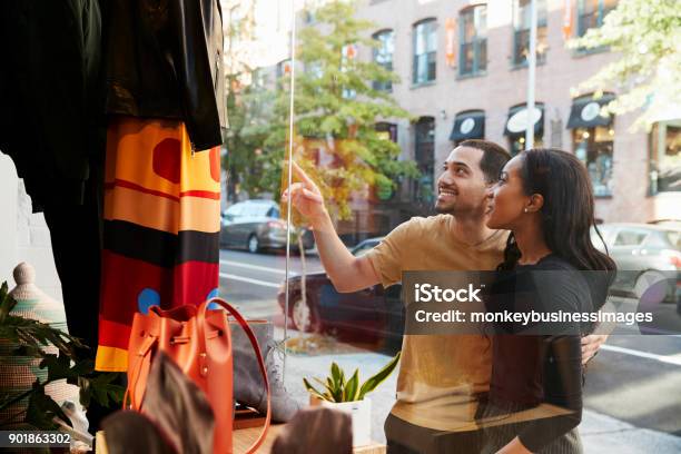 Smiling Couple Pointing At Clothes In A Shop Window Stock Photo - Download Image Now