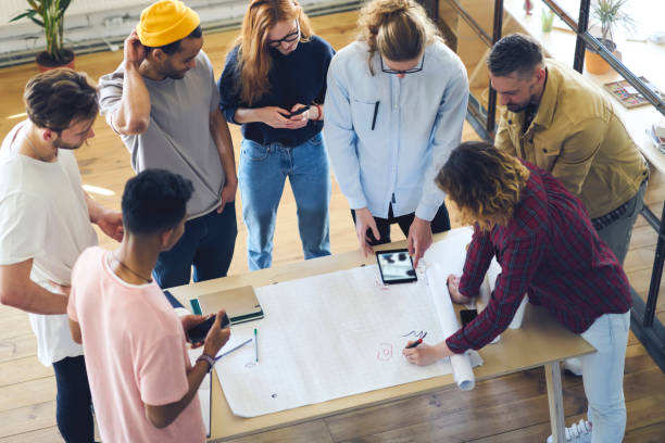 istock Dream team of skilled male and female architects having brainstorming session while drafting graphic blueprint during meeting table in modern loft studio, coworkers sharing ideas collaborating 901863400