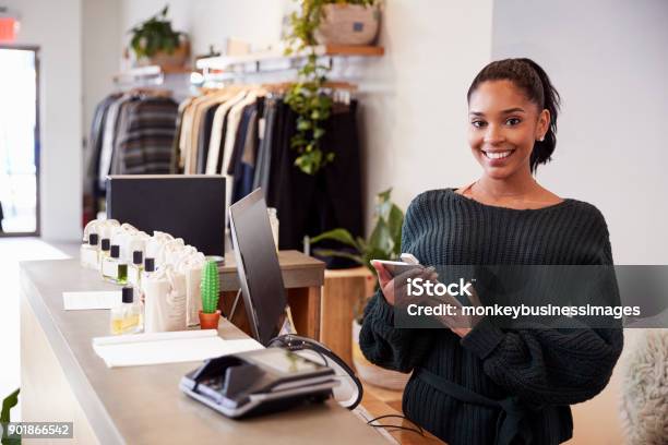 Female Assistant Smiling From The Counter In Clothing Store Stock Photo - Download Image Now
