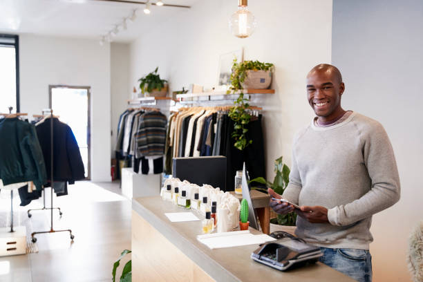 mężczyzna asystent uśmiecha się za ladą w sklepie odzieżowym - clothing store sales clerk usa clothing zdjęcia i obrazy z banku zdjęć