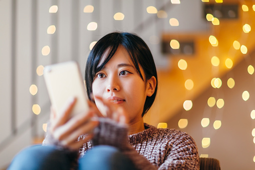 A young Japanese woman is using a smart phone while relaxing at home.