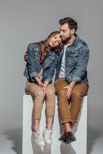 beautiful young couple in love sitting together on grey