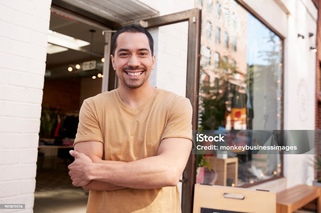 若いヒスパニック系店のオーナーは彼の店の外のカメラに笑顔 - ラテンアメリカ人およびラテン系アメリカ人のロイヤリティフリーストックフォト