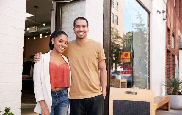 Young Hispanic couple smiling to camera outside their shop Young Hispanic couple smiling to camera outside their shop hand on shoulder photos stock pictures, royalty-free photos & images