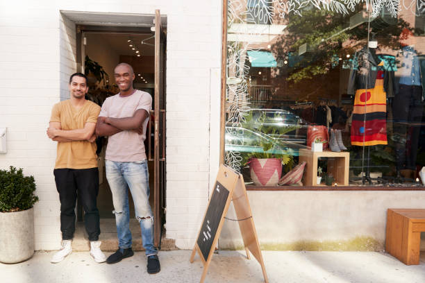 zwei junge männer, lächeln und kamera außerhalb ihrer kleidung shop - full length windows stock-fotos und bilder