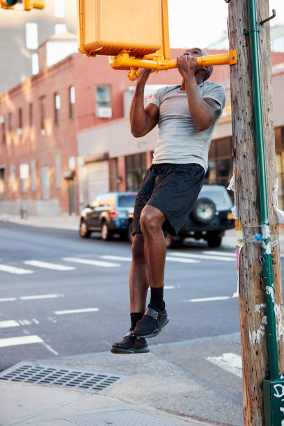 istock Young black man doing chin ups in Brooklyn street, vertical 901870318