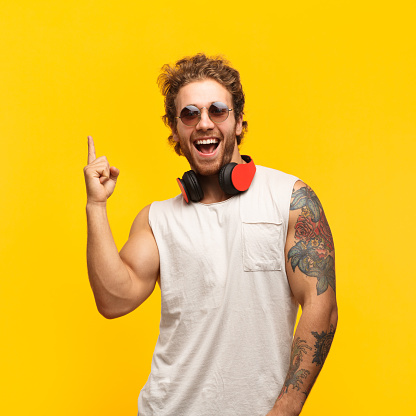 Cheerful man with headphones standing on yellow background and pointing up with index finger.