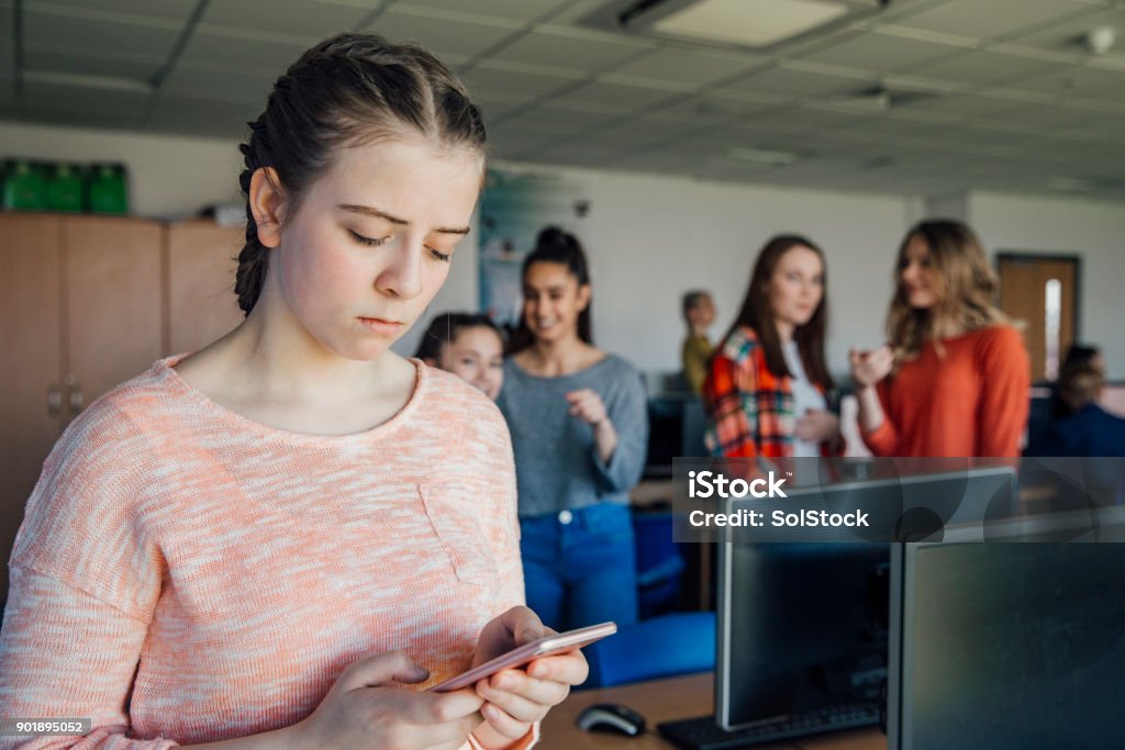 Teenage Girl Being Bullied By Text Message A teenage student is the victim of cyber bullying, looking sad Bullying Stock Photo