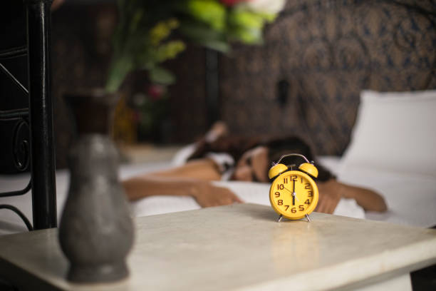 Alarm clock with woman sleeping on bed in the background