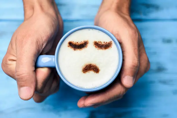 Photo of man with a cup of cappuccino with a sad face