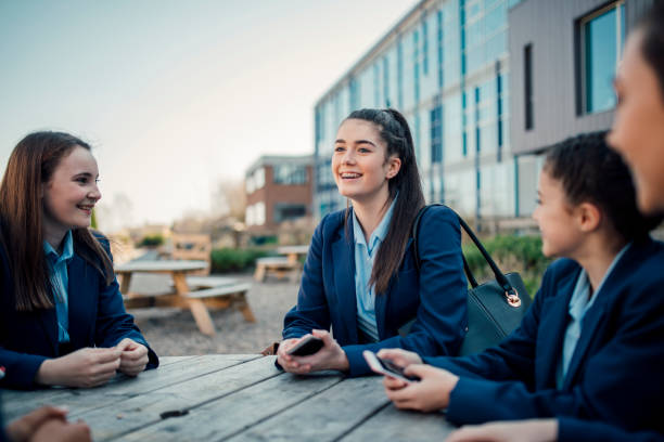 Breaktime At School A group of schoolgirls sit talking at a table outside of school school uniform stock pictures, royalty-free photos & images