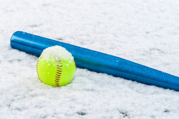um softball amarelo e bastão de alumínio azul sentado na neve - softball playing field fluorescent team sport - fotografias e filmes do acervo