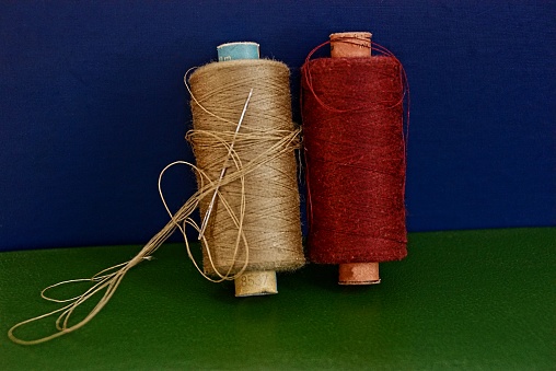 Brown and red thread with a needle on a blue green surface