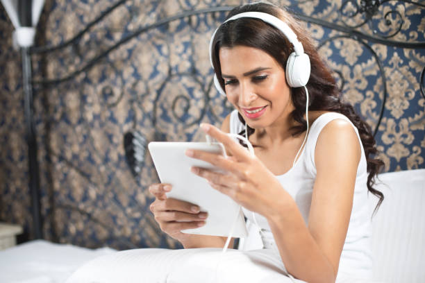 istock Happy woman using digital tablet and headphones in bed 901924700
