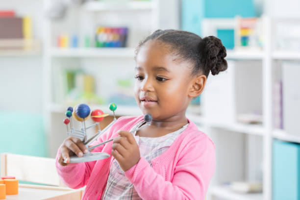 istock Little girl enjoys examining solar system model in preschool 901926534