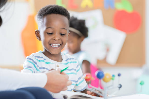 istock Little boy looks at a book with day care worker 901926538