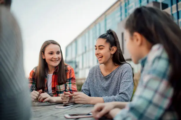 A group of schoolgirls sit talking at a table outside of school