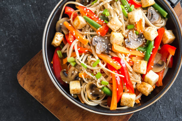 Stir fry with noodles, mushrooms and vegetables Stir fry with udon noodles, tofu, mushrooms and vegetables. Asian vegan vegetarian food, meal, stir fry in wok over black background, copy space. stir fried stock pictures, royalty-free photos & images