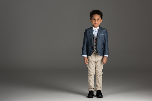 adorable african american boy standing in suit on gray