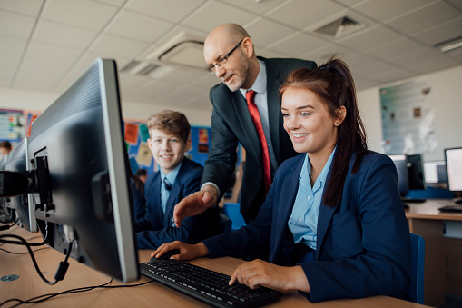 Two pupils are sitting behind computers receiving help in a lesson