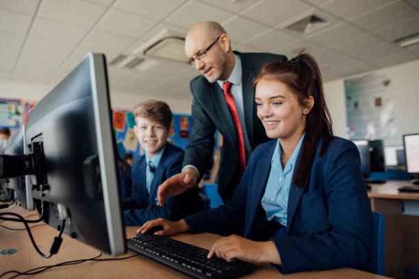 Receiving Help In A Lesson Two pupils are sitting behind computers receiving help in a lesson uniform stock pictures, royalty-free photos & images