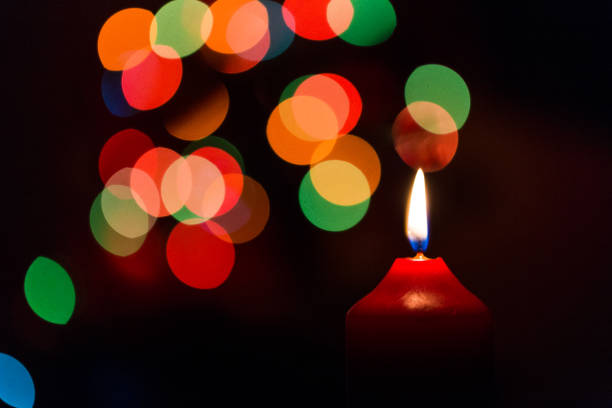 istock Burning red candle with multi colored bokeh and black background 901978046