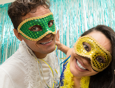 Two friends are posing for the party photo. Couple uses Carnaval masks in Brazil, they look at the camera.