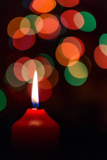 istock Burning red candle with multi colored bokeh and black background 901980980