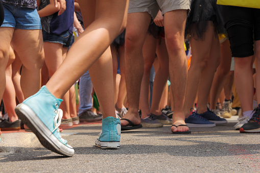 Teenage woman is dancing in street party, Carnaval. Camera low angle, many anonymous legs in a crowd. All people wear shorts. Summer. Outdoor party, movement, fun, relaxation.