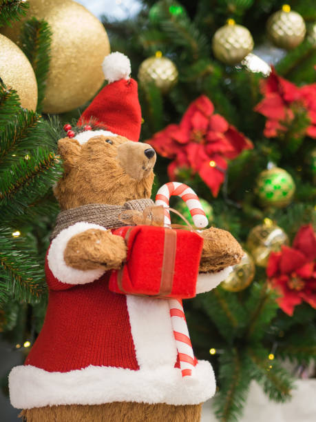 istock A toy bear dressed as a Santa Claus standing against a Christmas tree holding a gift box. Christmas and New Year concept. 901995202