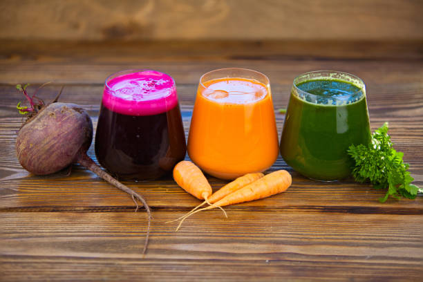 три овощных сока в стеклянной чашке на деревянном фоне - carotene стоковые фото и изображения