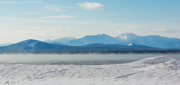 frigid winter morning with misty steam rising off the lake with the Adirondack mountains across the lake in New York