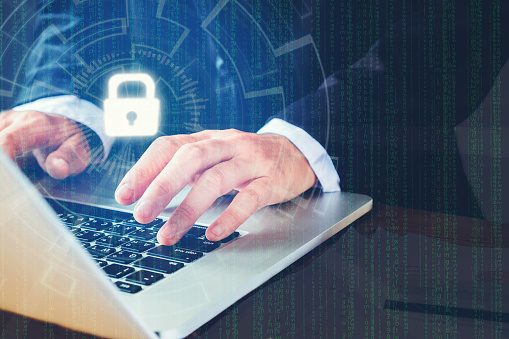 A person in a formal suit is typing on a laptop, with a digital lock icon displayed above the keyboard and matrix-like code in the background, symbolizing cybersecurity.