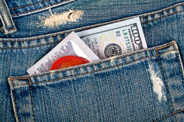 préservatif rouge et cent dollars dans une poche de jeans bleu - sex condom jeans horizontal photos et images de collection