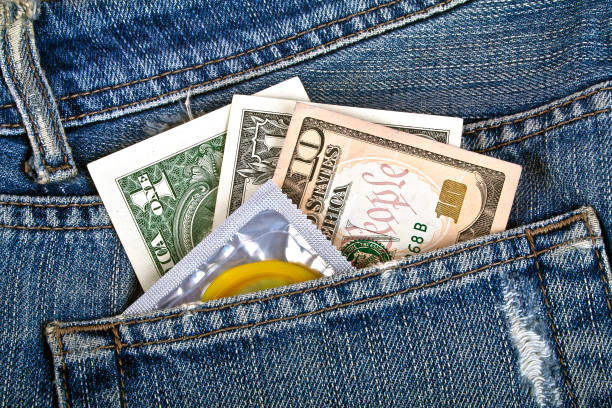 préservatif jaune et des dollars américains dans une poche de jeans bleu - sex condom jeans horizontal photos et images de collection