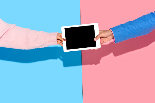 Cropped image of hands holding digital tablet on pink and blue background