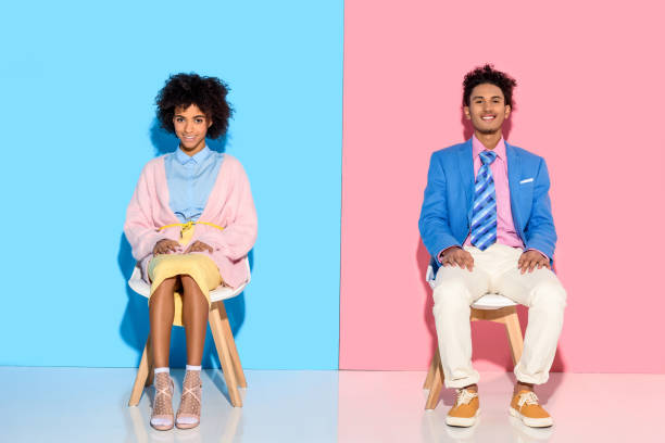 istock couple sitting on chairs against pink and blue wall backdrop 902145044