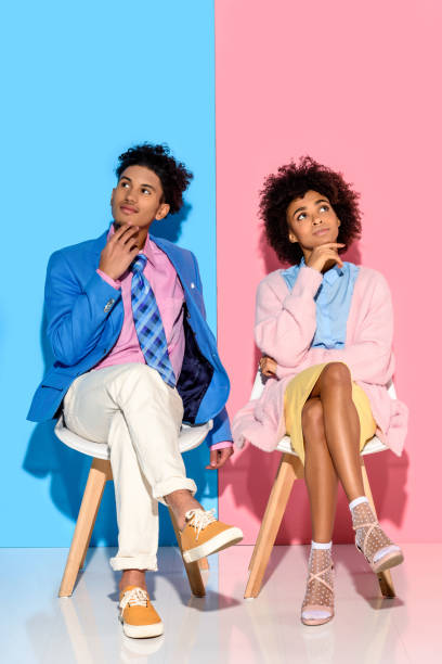 istock couple sitting on chairs against pink and blue wall backdrop 902145076
