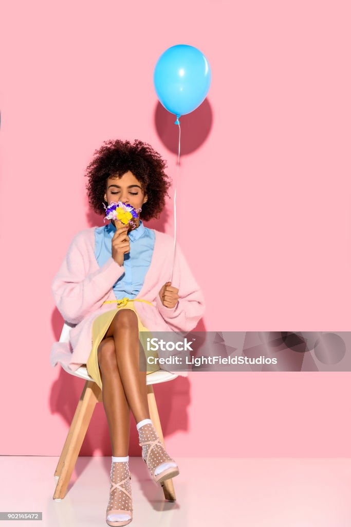 woman with flowers in ice cream cone and balloon african american woman with flowers in ice cream cone and balloon in hands on pink wall backdrop Women Stock Photo