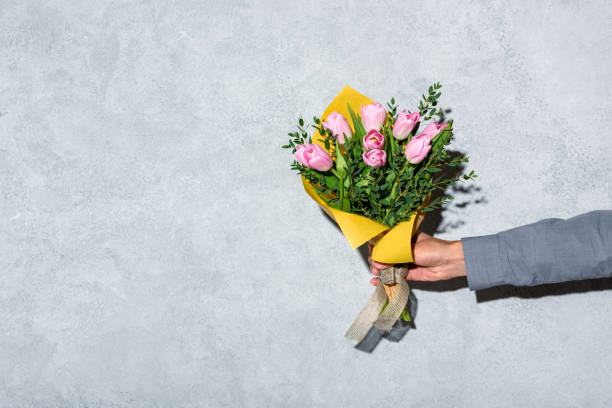 istock man giving bouquet of flowerson grey background 902149954