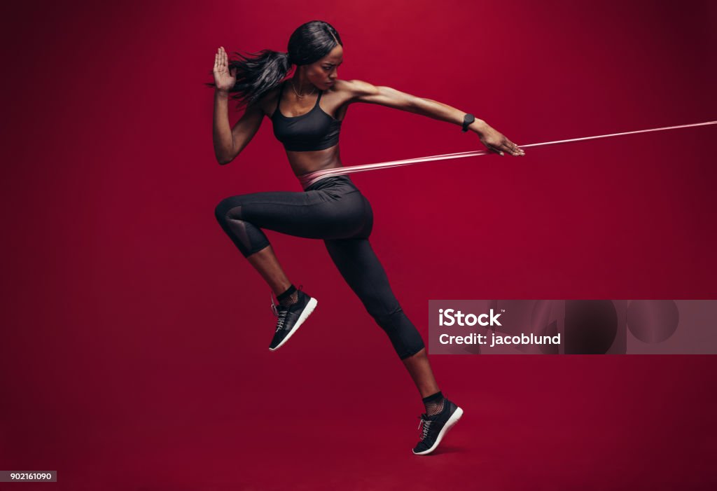 Sporty woman exercising with resistance band Sporty woman exercising with resistance band on red background. African female athlete working out with elastic bands in studio. Resistance Band Stock Photo