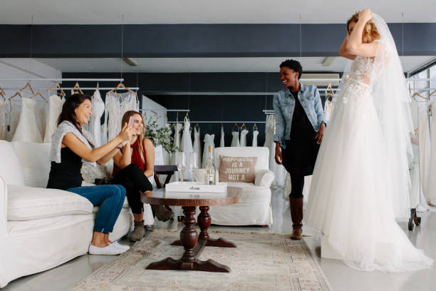 Woman trying on wedding dress in a shop with friends Woman trying on wedding dress with female friends having fun and taking photographs. bridal shop photos stock pictures, royalty-free photos & images