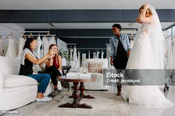 Woman Trying On Wedding Dress In A Shop With Friends Stock Photo - Download Image Now