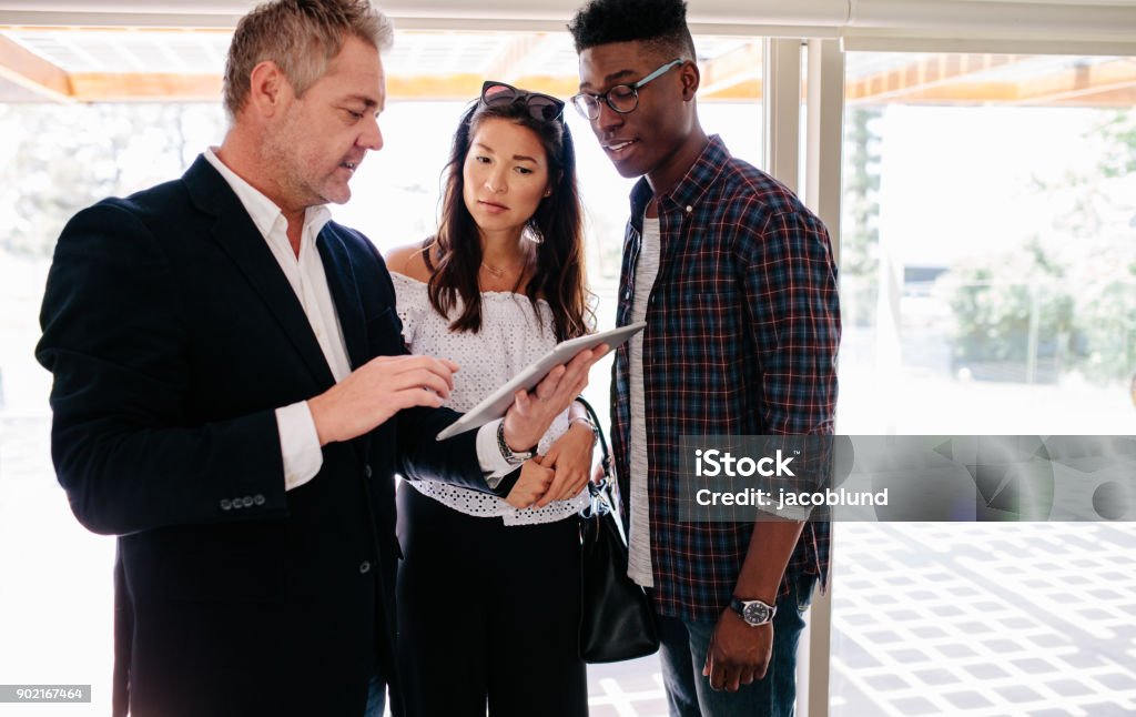 Real Estate Agent sharing property details with clients Real Estate Agent showing terms of contract on tablet to interracial couple. Real estate agent sharing property details with clients. Real Estate Agent Stock Photo